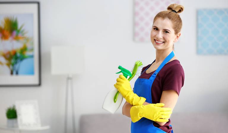 Smiling woman in yellow glove holding a white bottle with green cap and a green brush in her hand.