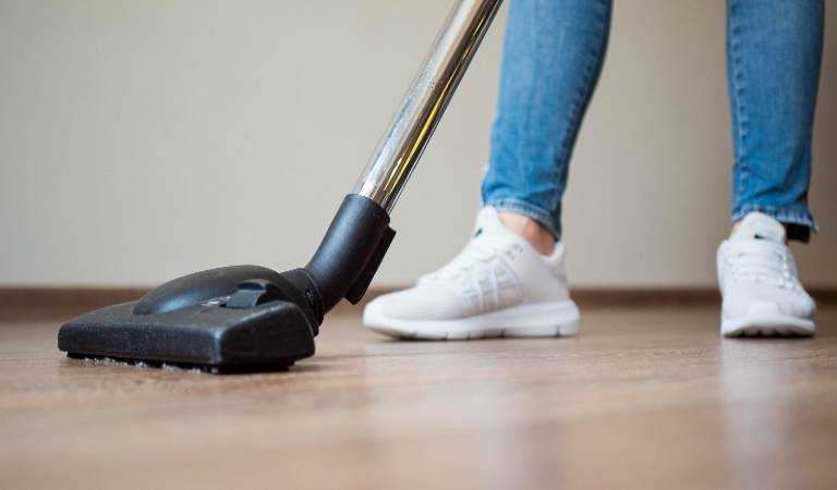 Leg in blue jeans and white shoes with a steam mop on the floor.