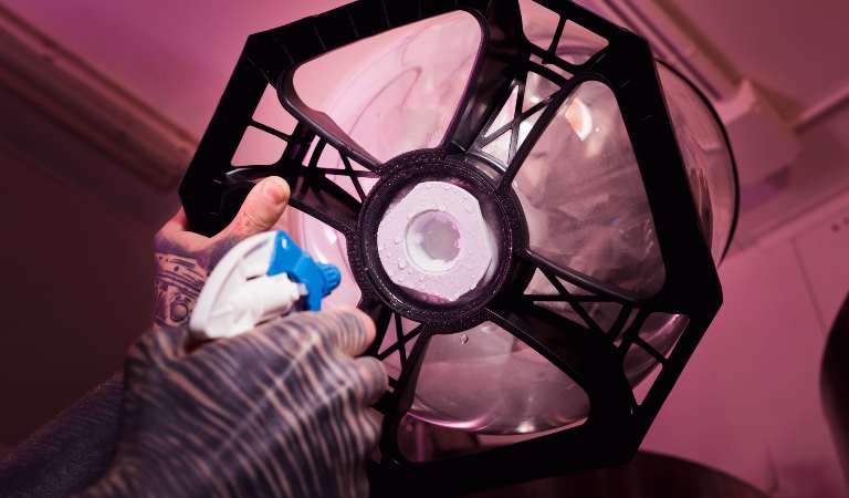 Hand of a man in gloves holding a bottle and cleaning glass light fixture.