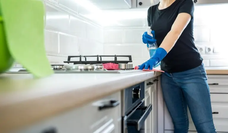 Lady in black top and blue jeans cleaning inside her kitchen.