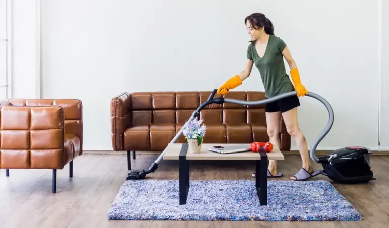 A lady is using vacuum cleaner on floor inside a living room.