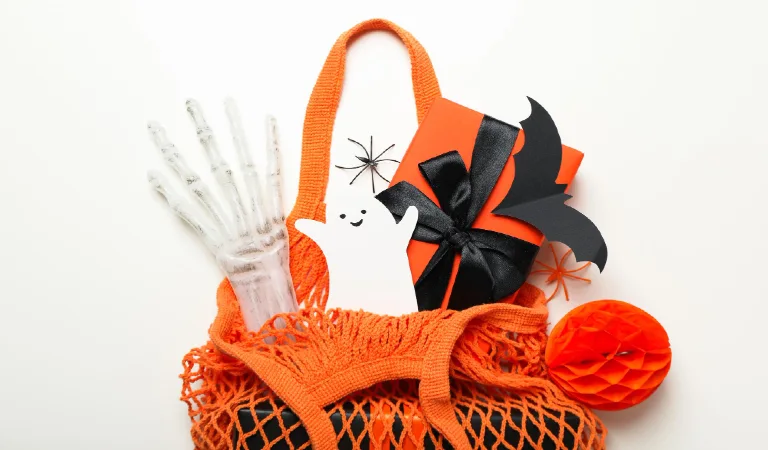 Gift box and paper ghost and bat in shopping bag on white background top view