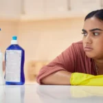 Cleaning spray bottle and frown with an annoyed woman housekeeper looking at hygiene products