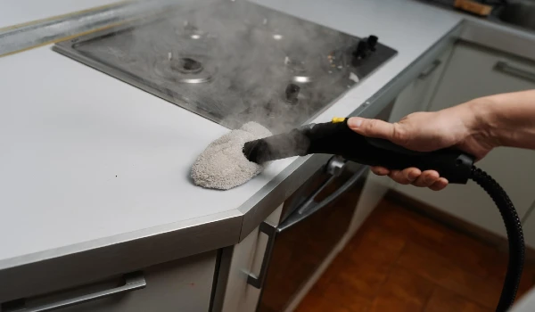 Closeup cropped shot of unrecognizable man brushing kitchen countertop with steam cleaner promoting