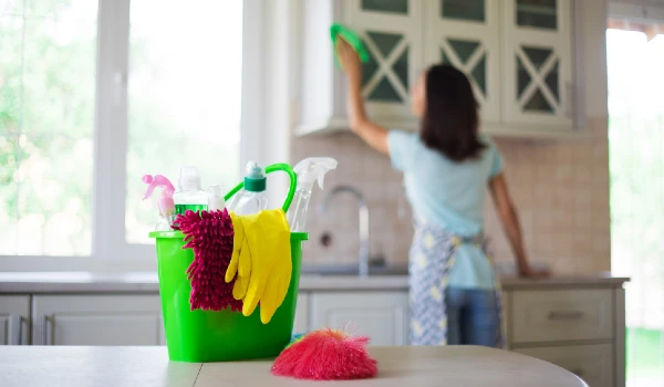 Young woman in yellow gloves is cleaning the kitchen with special equipment and spray